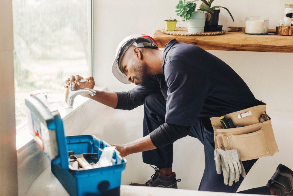 Engineer inspecting tap in bathroom with toolkit nearby